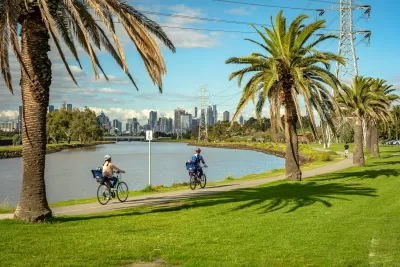 Two people on bikes on a riverbank trail in Melbourne, Australia with city skyline in background