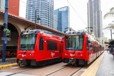 Two red San Diego trolley cars at Santa Fe Depot station with high-rise buildings in background.
