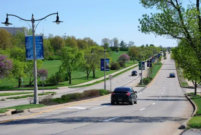 Wide suburban road with landscaped median and light pole banners advertising local amphitheater.