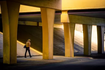 Man in wide-brimmed hat walks through nondescript concrete freeway underpass.