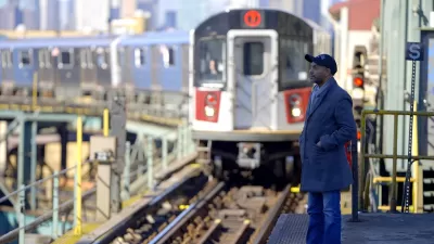 Subway train pulling into elevated outdoor platform in New York City with one passenger waiting.