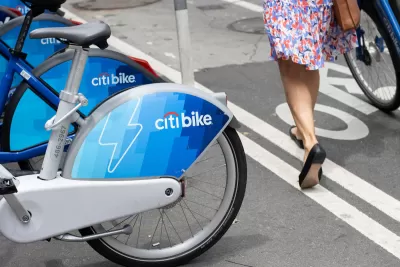 Close-up of Citi Bike electric bikes at on-street station in New York City next to bike lane with woman walking a bike.