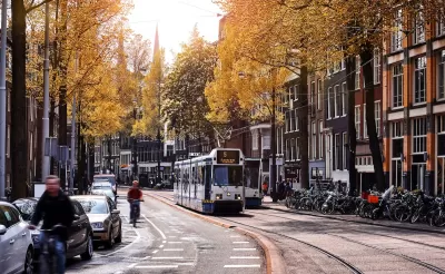 Tram and cyclist on Amsterdam street with sunrise or sunset in background.