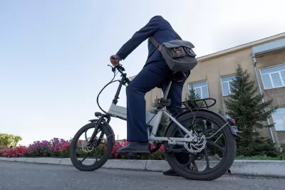 Person on folding electric bike wearing messenger bag resting foot on ground on urban street.