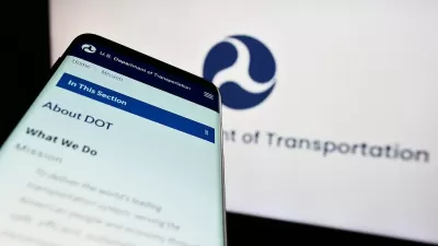 Close-up of smartphone with USDOT website pulled up and screen with USDOT logo in background.