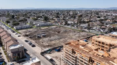 Aerial view of large construction site and vacant, graded lot next to public housing buildings in Watts, Los Angeles, California.