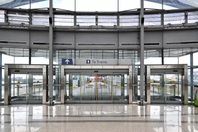 View of large glass building with glass doors and "To Trains" sign.