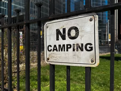 Close-up of white and black NO CAMPING sign on black iron fence.