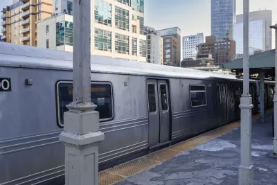 Silver train at station on elevated track with city high-rises in the background.