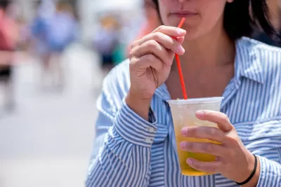 Close-up of woman in blue and white striped button-up shirt drinking from clear plastic cup with red straw.