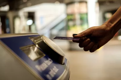 Close-up of hand holding transit card up to fare collection machine in transit station.