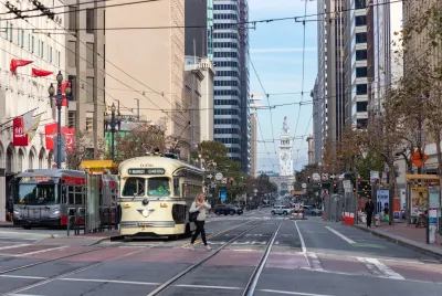 Streetcar and bus stopped at station on Market Street in San Francisco with Ferry Building visible in background.