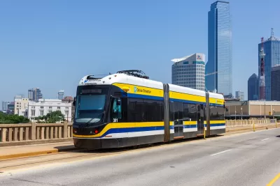 White and yellow DART streetcar on bridge in Dallas, Texas with skyscrapers in background.