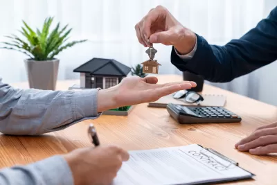 Close-up of person signing home or apartment contract and receiving house key with house-shaped keychain.