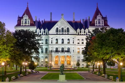 New York state capitol building with green lawn and statue in front at dusk.