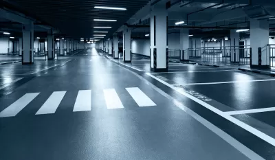 Black and white tinted photo of underground parking garage with black floor, white crosswalk, and harsh lighting.
