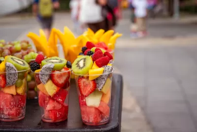 Close-up of rows of clear plastic cups filled with cut fruit on outdoor street vendor table
