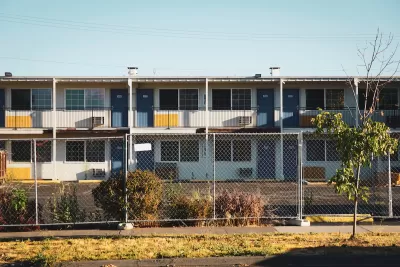 Closed, boarded-up two-story motel behind chain-link fence.