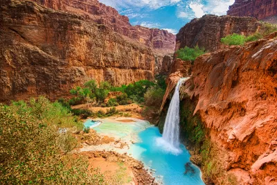 View of Havasu Falls with bright turquoise water and a canyon winding through red vertical cliffs in the Grand Canyon