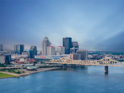 Louisville, Kentucky skyline with river and bridge in foreground at dusk.