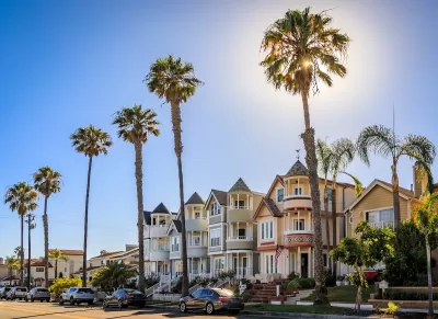Historic Victorian homes in Huntington Beach, California with tall palm trees on a sunny day.