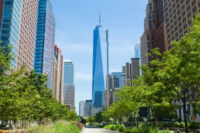 View of One World Trade Center down straight street with bright green trees on either side.