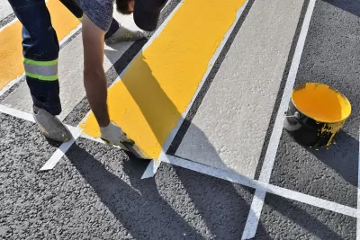 Close-up of man painting white and yellow crosswalk on asphalt.