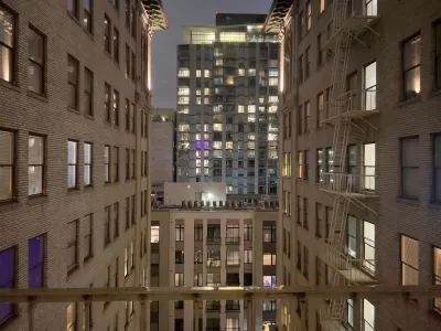 View from between tall white brick buildings in evening in downtown Los Angeles with modern office building across street.
