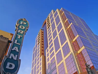 View looking up at vintage neon PORTLAND sign and modern high-rise building in Portland, Oregon.