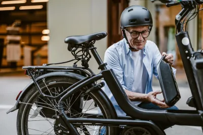 Man wearing black bike helmet changing battery on black e-bike outdoors.