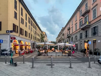 Pedestrianized street in Milan, Italy with outdoor dining tables and umbrellas.