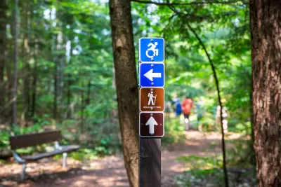 Sign showing accessible hiking trail sign with blurred forest in background.