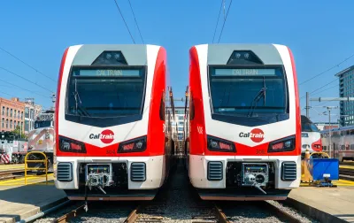 Two white and red Stadler electric Caltrain trains next to each other on a sunny day.