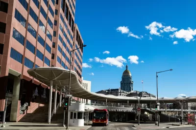 Red bus parked at transit station in Denver, Colorado with CO state capitol dome in background.