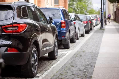 Curbside packed with park cars and cyclist riding on the sidewalk.