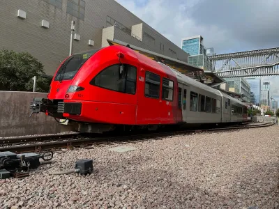 Red modern train on tracks with large warehouse-type building behind it in Austin, Texas.