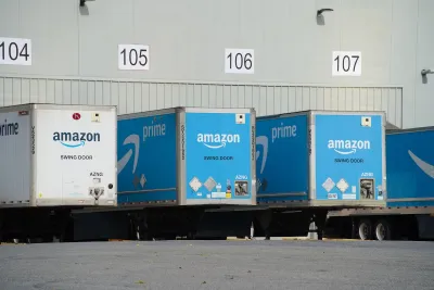 Blue and white Amazon trucks parked at loading docks at warehouse.