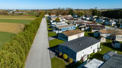 Aerial view of mobile home community in rural area with homes lined up diagonally next to small road.