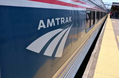 Close-up of Amtrak logo on blue passenger train stopped at outdoor station platform.