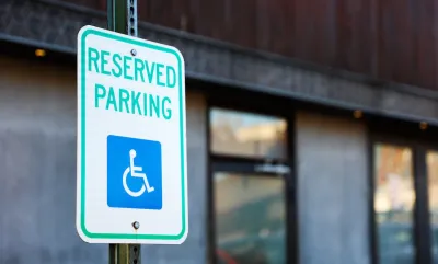 Close-up on white sign with green "Reserved Parking" letters and blue accessibility symbol.
