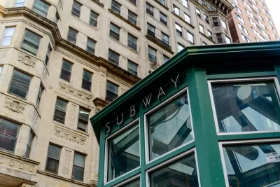 Green subway station entrance kiosk with brick buildings in background.