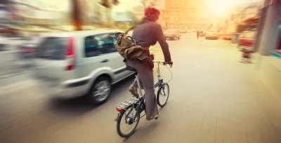 Cyclist on folding bike riding next to silver car on city street.
