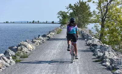 View from behind of woman wearing helmet on bicycle riding on concrete causeway with water on either side.