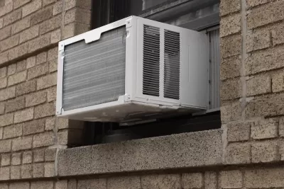 Close-up of white air conditioning window unit in window of brown brick building.