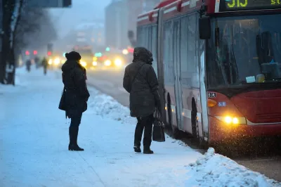 Two people waiting to board arriving bus on a snowy day.