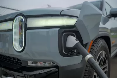 Close-up of front corner of grey Rivian truck with charger plugged in.