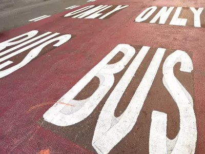 White BUS ONLY letters on red painted bus lane on street.