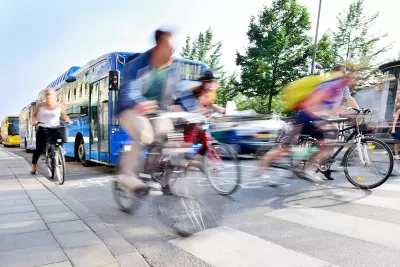 Blurred bicyclists riding through crosswalk with blue bus behind them.