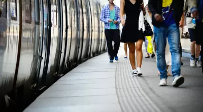 Low shot of side of subway or commuter train and passengers walking on platform next to it.