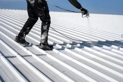 Worker painting metal roof white.